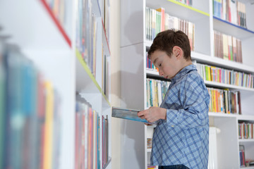 Naklejka na ściany i meble Cute boy reading book in library 
