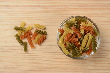 Pasta espirales de tres colores en un bol de cristal sobre fondo de madera