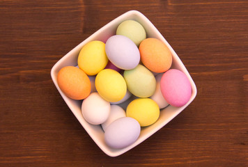 Colored eggs on a square bowl on wooden table top views