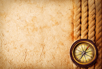 Ancient brass compass with rope on vintage old paper background. Retro stale.