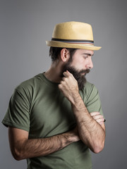 Profile view of sad bearded man wearing straw hat looking away.  Headshot portrait over gray studio background with vignette. 