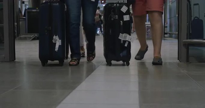 Three People With Big Roll-on Bags Walking Out Of Airport Terminal Through The Automatic Doors