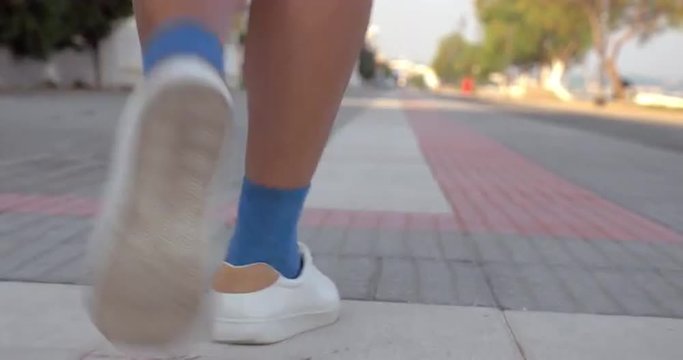 Steadicam shot of senior woman in blue socks and white sport shoes speed walking along the water front. Active and healthy lifestyle