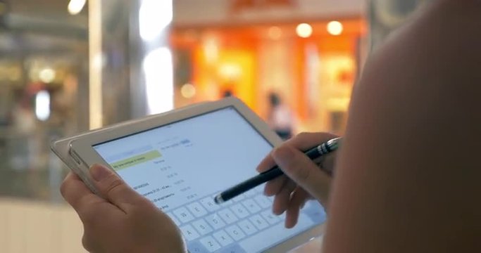Close-up shot of a woman typing message or taking notes on tablet computer at the airport of shopping mall
