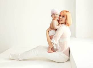 Happy mother with baby home in white room near window