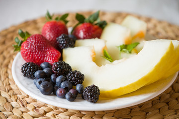 Cut melon and berries. Fruit salad of strawberries, blueberries, melon, mint and blackberries. Diet salad on the white plate - breakfast, weight loss concept. closeup. Healthy snack.