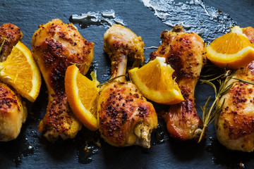 Roasted chicken legs, orange and rosemary on the black background. Cooked with sauce from mustard, orange, honey and olive oil. - 106433210