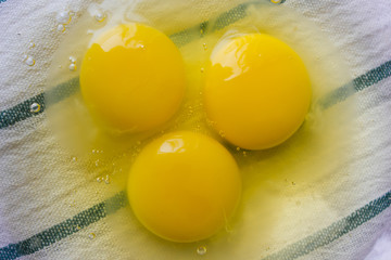 three raw eggs in a transparent bowl on a light background