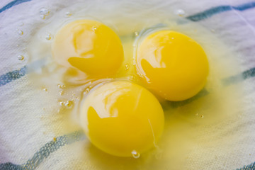 three raw eggs in a transparent bowl on a light background