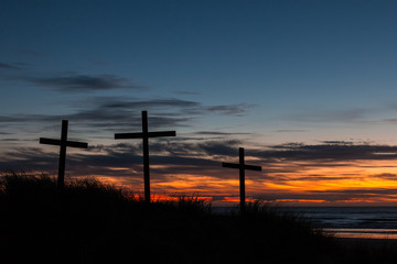 Three crosses on a sand dune with a sunset over the sea.