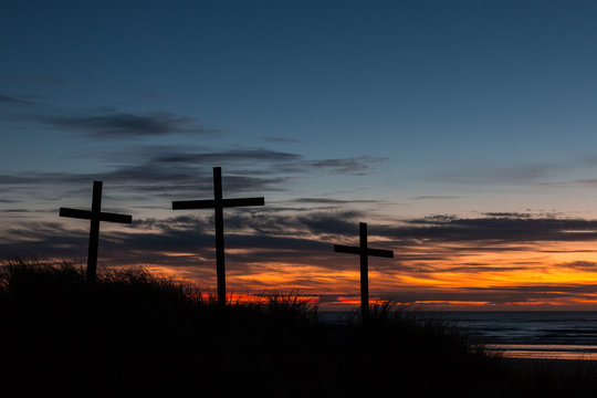 Three crosses on a sand dune with a sunset over the sea.