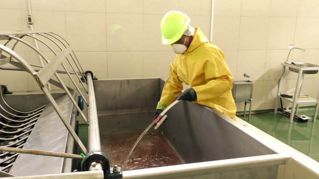 A worker in full protective gear diligently cleans a scalding tub within the premises of a slaughterhouse,ensuring utmost hygiene and safety.