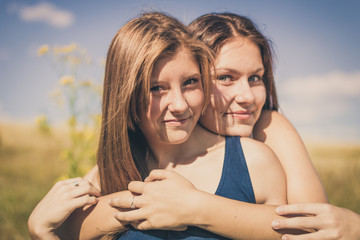 Two happy smiling girls hug over blue sky