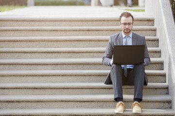 Businessman in suit sitting on the stairs and working on laptop outdoors    