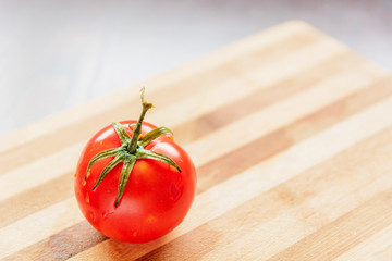 large and red tomato with green leaves on a bamboo board