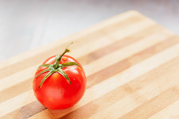 large and red tomato with green leaves on a bamboo board
