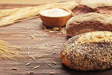 Fresh baked bread, a bowl of flour and wheat ears on the wooden background