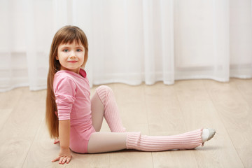 Little cute girl in pink leotard sitting on floor at dance studio