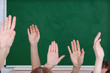 Raised hands on blackboard background in class