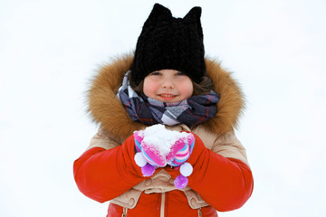 Little girl with winter clothes holding snow in hands outdoor, close up