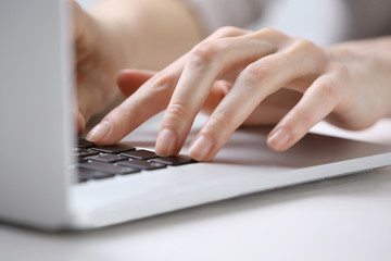 Female hands using laptop on white wooden table, close up