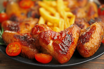 Grilled chicken wings with French fries, garden-staff and tomatoes on plate