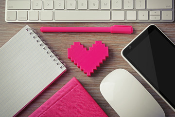 Computer peripherals with pink heart, notebooks and mobile phone on wooden table
