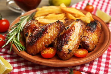 Baked chicken wings with French fries on brown plate