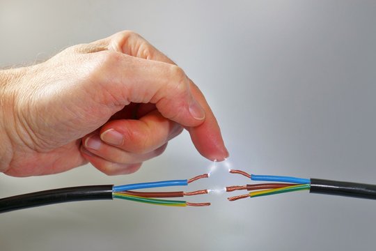 Hand greift in Kabel, Stromschlag durch Funkenblitz