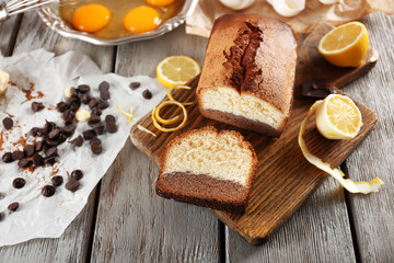 Fototapeta na wymiar Composition of tasty cake with broken eggs and lemon on grey wooden background