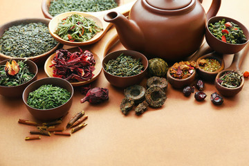 Variety of dry tea in bowls with teapot on light brown background, closeup