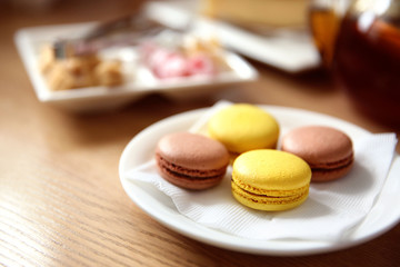 Fresh tasty macaroons on plate in cafe, close up