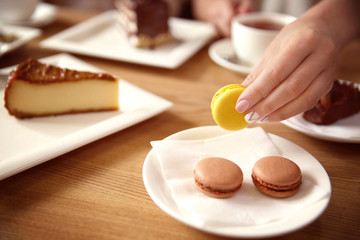 Woman holding fresh tasty macaroons on plate in cafe, close up