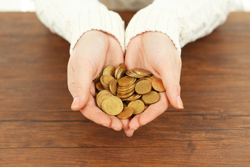 Young woman in a white knitted sweater holding a heap of  coins in her hands above  wooden table, close up