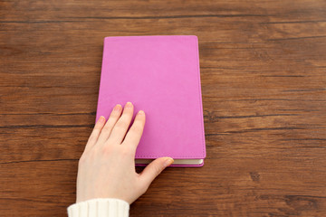 Obraz premium Female hand holding a purple book cover on the brown wooden desk, top view