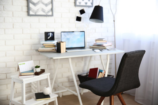 Workplace with laptop, table, lamp and chair in light room
