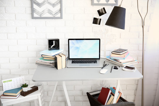 Workplace with laptop, table and lamp in light room