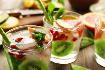 Refreshing cocktails with ice, mint, pomegranate seeds and slices of fruits on wooden background