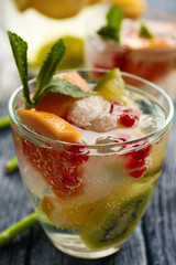 Refreshing cocktail with ice, mint, pomegranate seeds and slices of fruits on wooden background