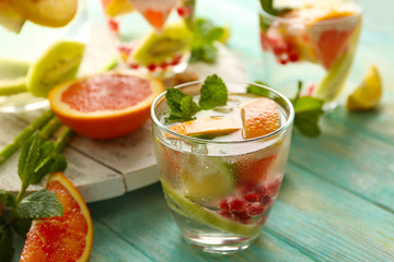 Refreshing cocktail with ice, mint, pomegranate seeds and slices of fruits on blue wooden background