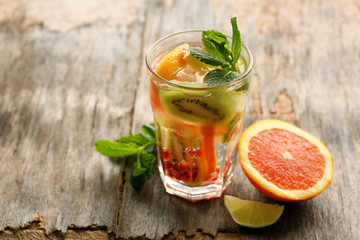 Refreshing cocktail with ice, mint, pomegranate seeds and slices of fruits on rustic wooden background