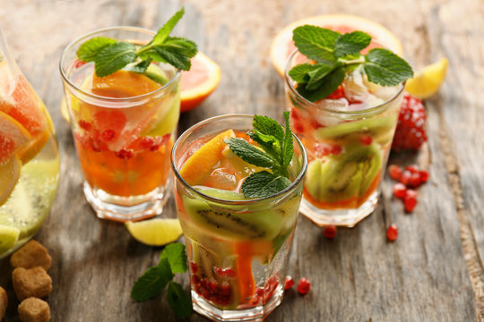 Refreshing cocktails with ice, mint, pomegranate seeds and slices of fruits on rustic wooden background