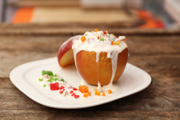Backed apple with cream, candied fruit and nuts on white plate