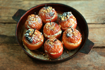 Baked apples with cottage cheese, raisins and walnut in pan on wooden table