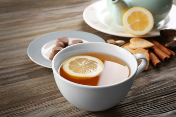 Cup of brewed tea with lemon and sweets on wooden table