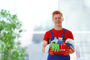 Young janitor holding cleaning products and tools on tub