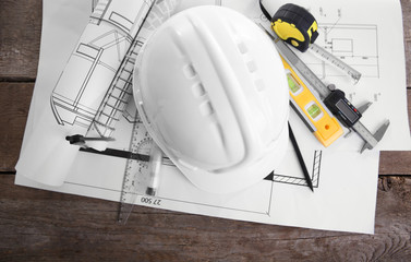 Yellow helmet and blueprints on a wooden background.