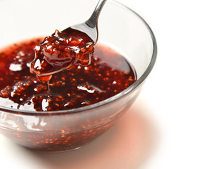 Sweet raspberry jam in the transparent glass bowl and tea spoon