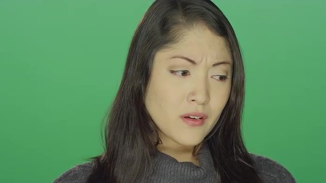 Beautiful young Asian woman starting to cry, on a green screen studio background