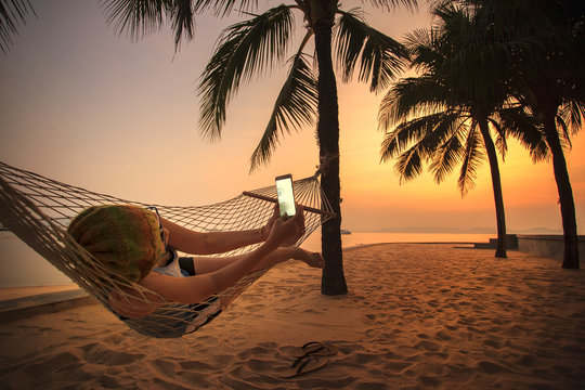 woman lying in beach cradle and taking a photograph by smart pho